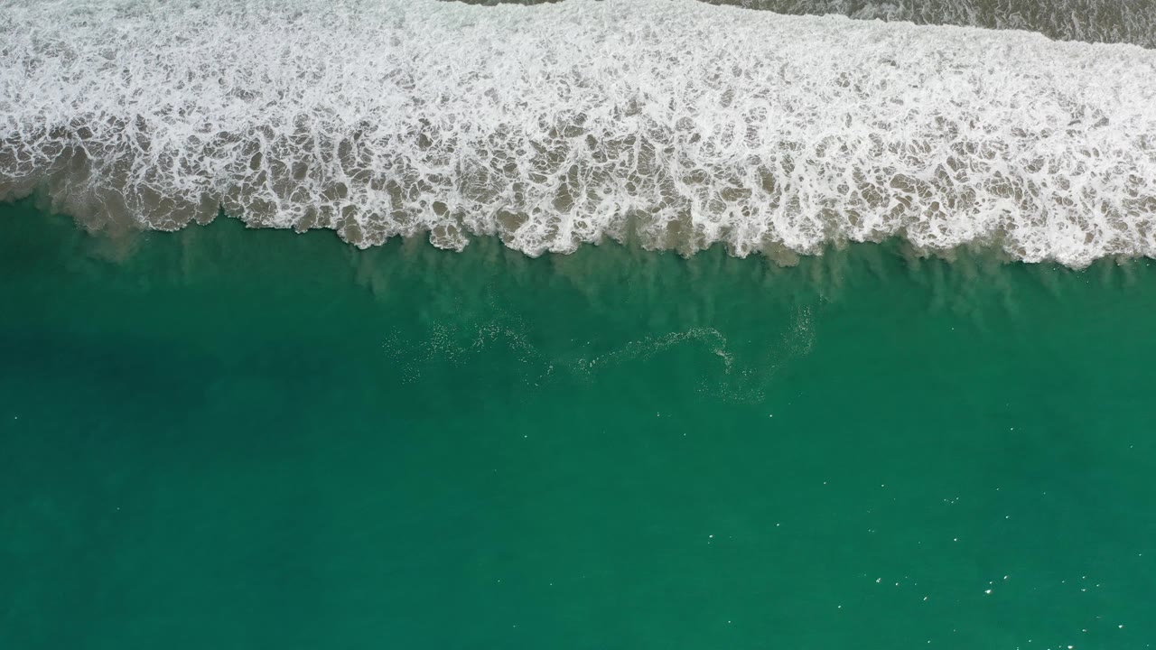 Top-down Los Cabos ocean frame with a broad white foam band crossing the top and darker green water below, with no visible people.
