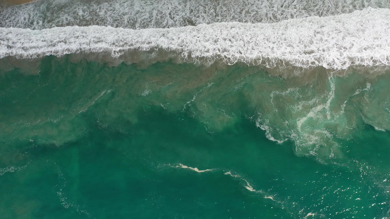 Overhead turquoise ocean with white surf breaking along sand
