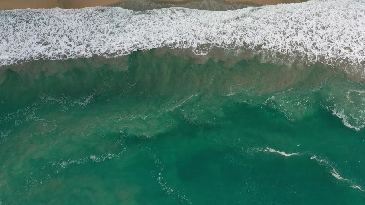 Overhead green surf breaking onto tan sand