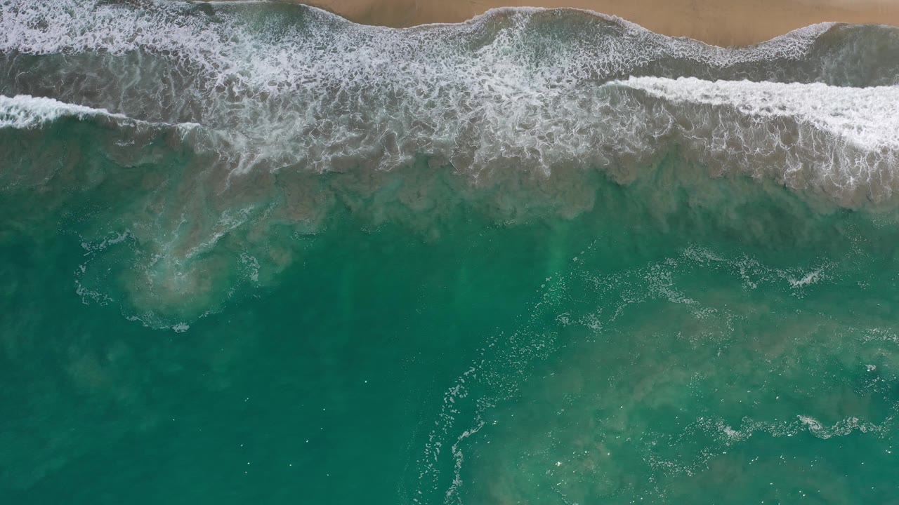Foamy surf spreads over shallow green water near sand