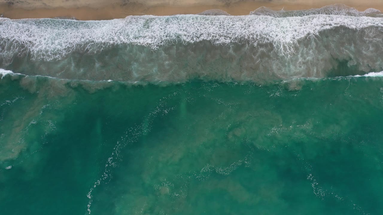 White breakers along sand above textured green ocean