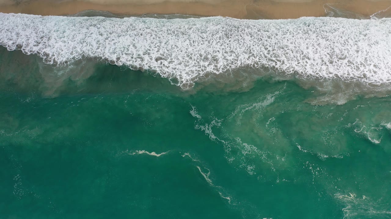 Aerial beach edge with foamy surf and clear green water
