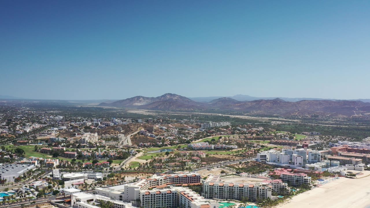 High aerial view of coastal buildings, beach, town, and mountains
