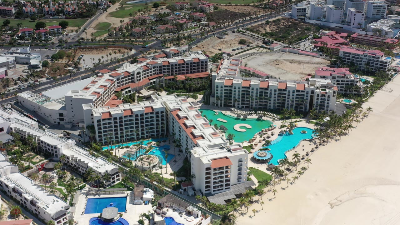 Oblique aerial of a large resort with multiple pools and beachfront sand.