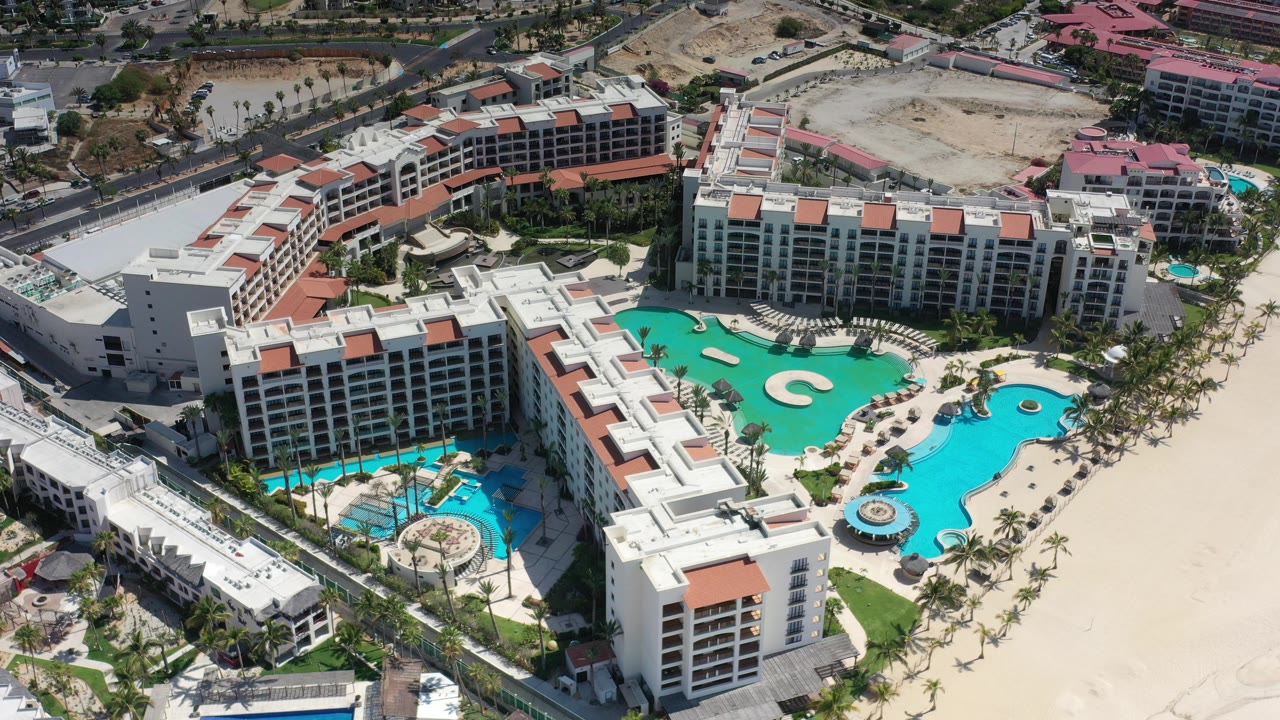 Aerial view of apartment buildings around turquoise pools and pale sand.