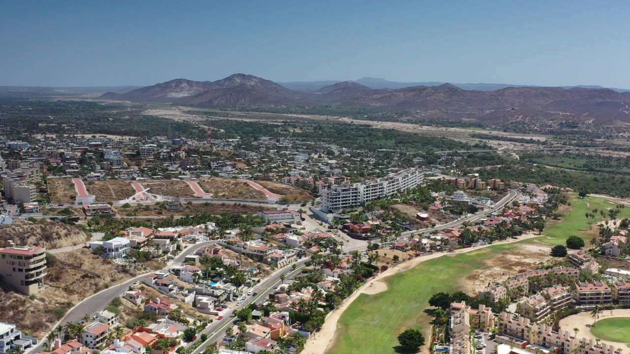 High aerial view of city buildings, green fields, roads, and distant hills.