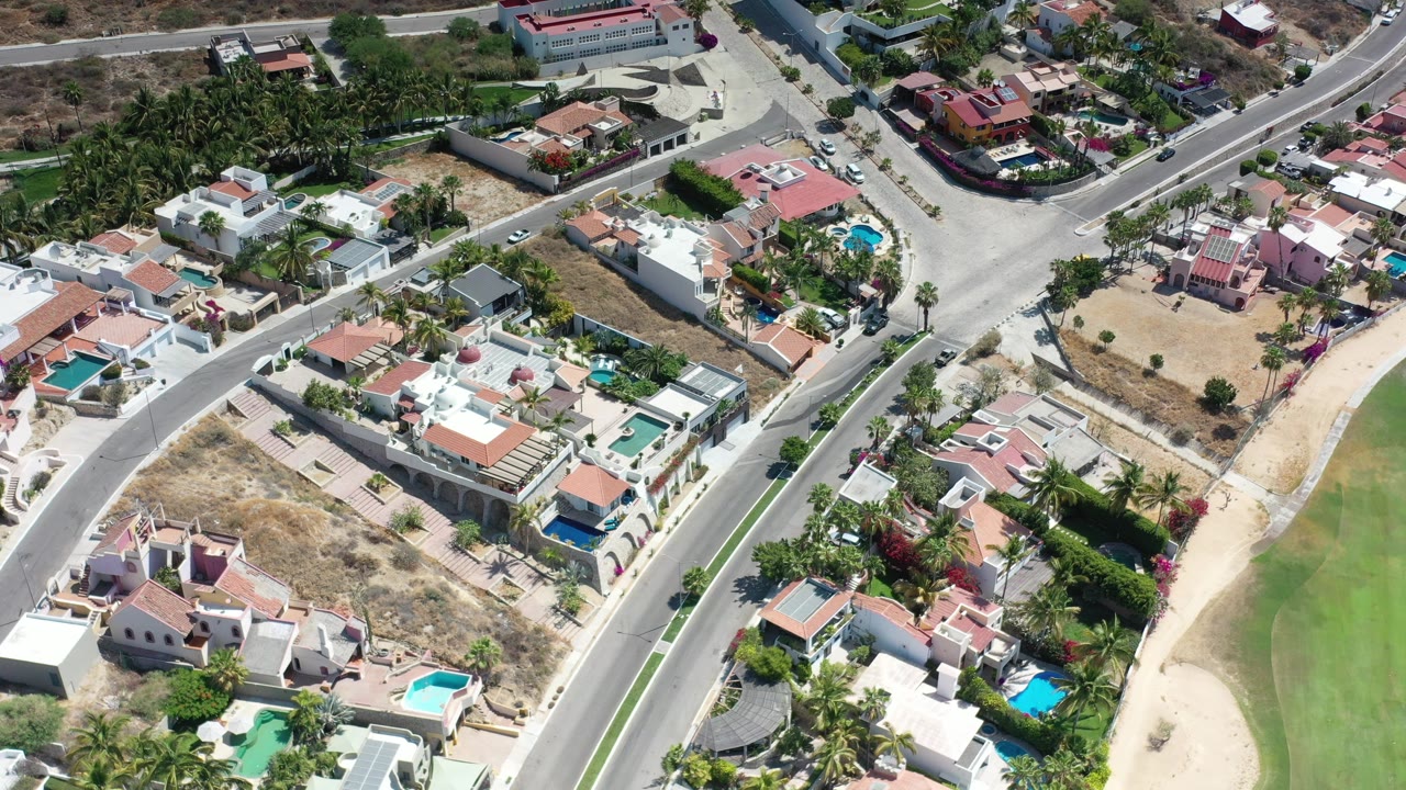 Aerial view of houses, roads, pools, and dry lots beside a green course