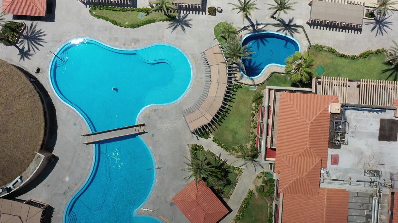 Overhead pool area beside sandy beach and red tile roofs.