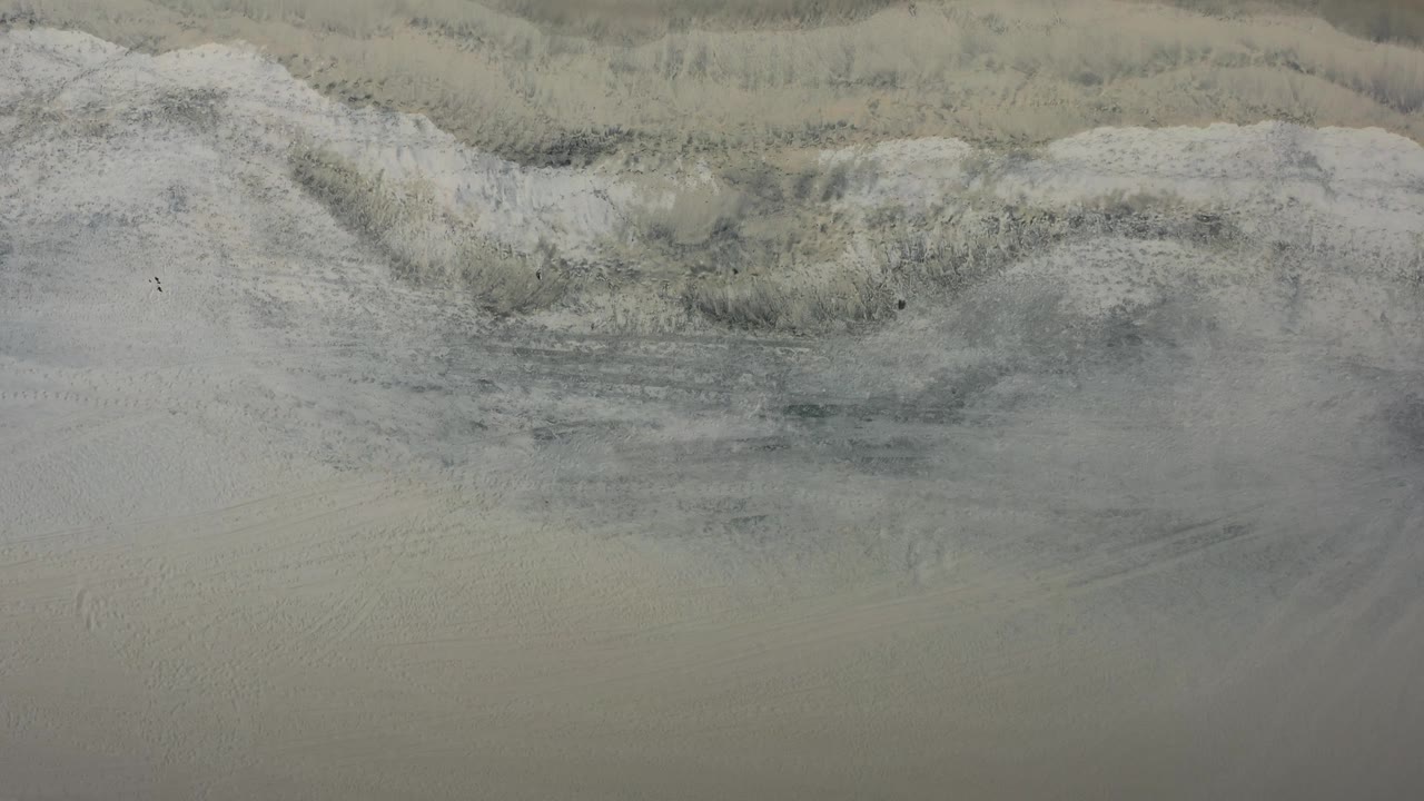 Top-down beach sand with subtle wave residue and a small dark object.