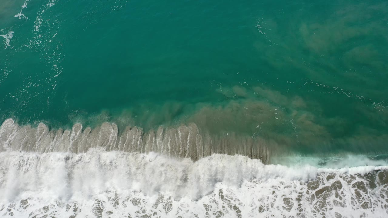 A thicker surf band breaks across clear green-blue water.
