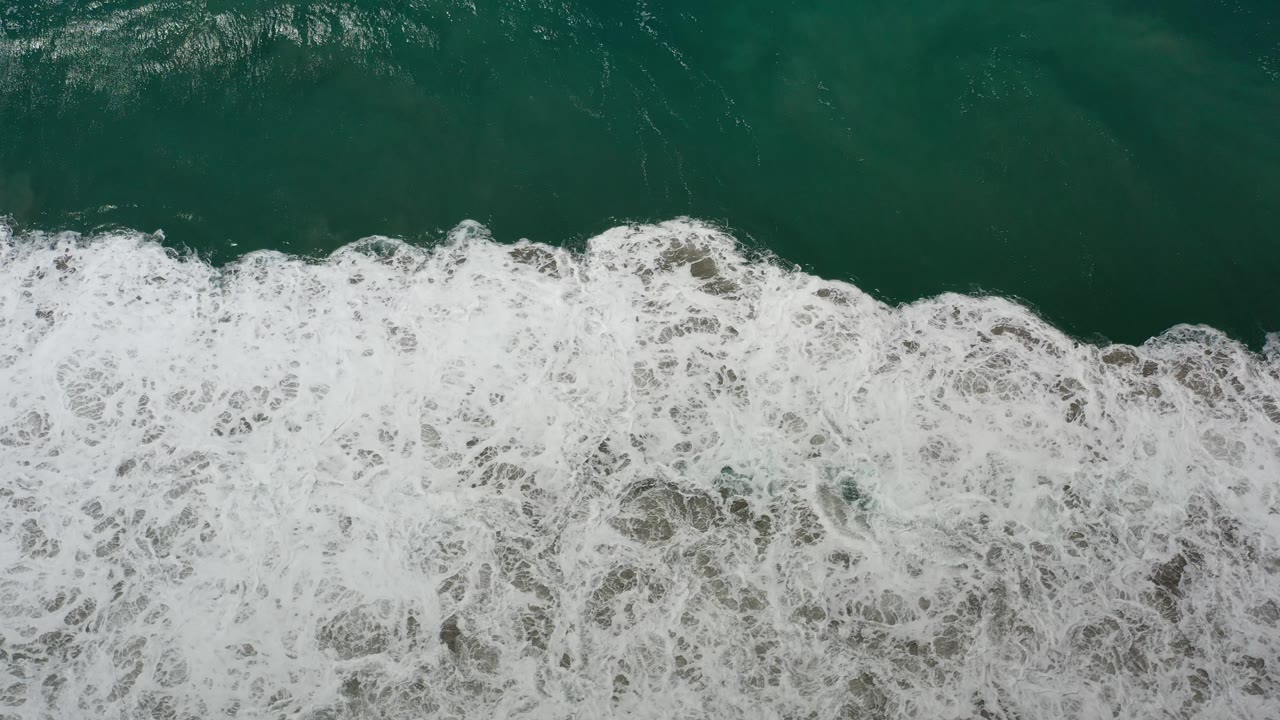 White wave foam advancing through green ocean water.