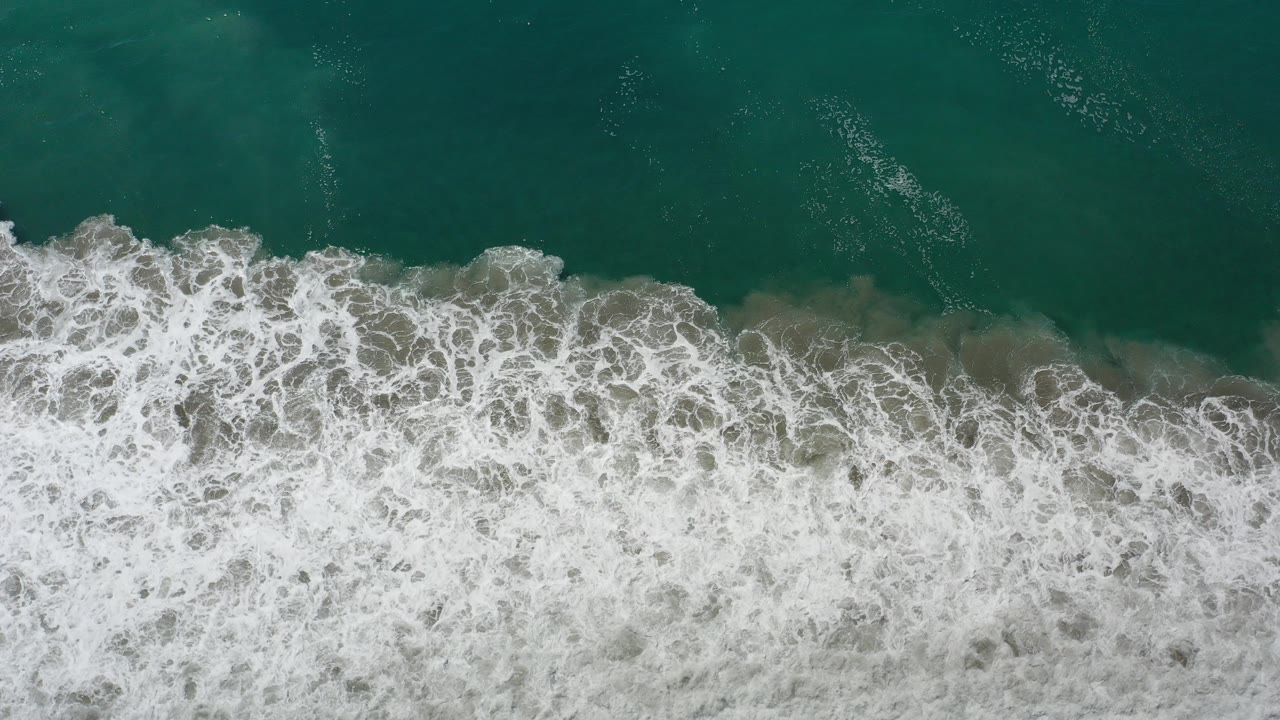 Overhead green water and white surf crossing sand