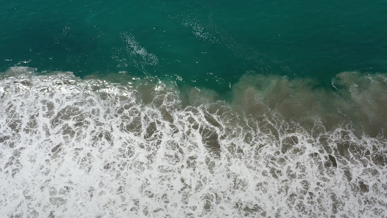 White surf foam rolls beneath green ocean water.