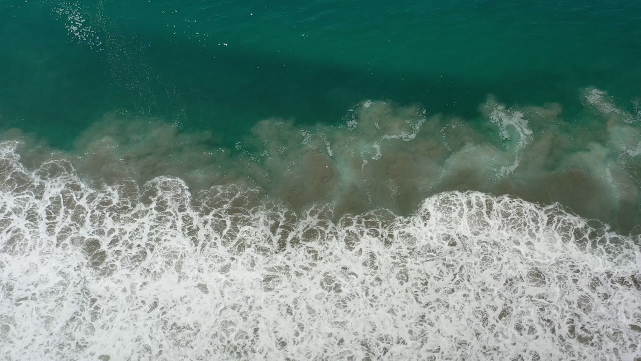 Aerial-style frame of Los Cabos green seawater, where a broad white foam band spreads through the lower half with no visible people.
