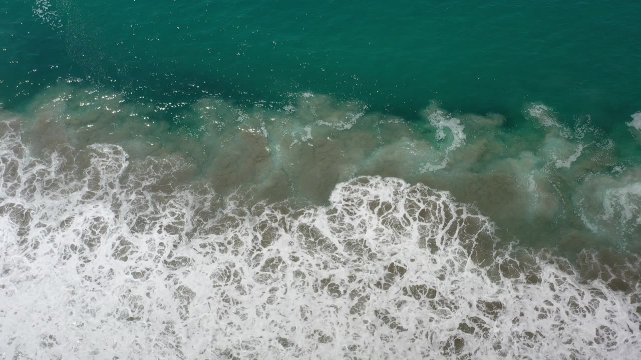 Overhead teal ocean water with white surf breaking over submerged rocks.