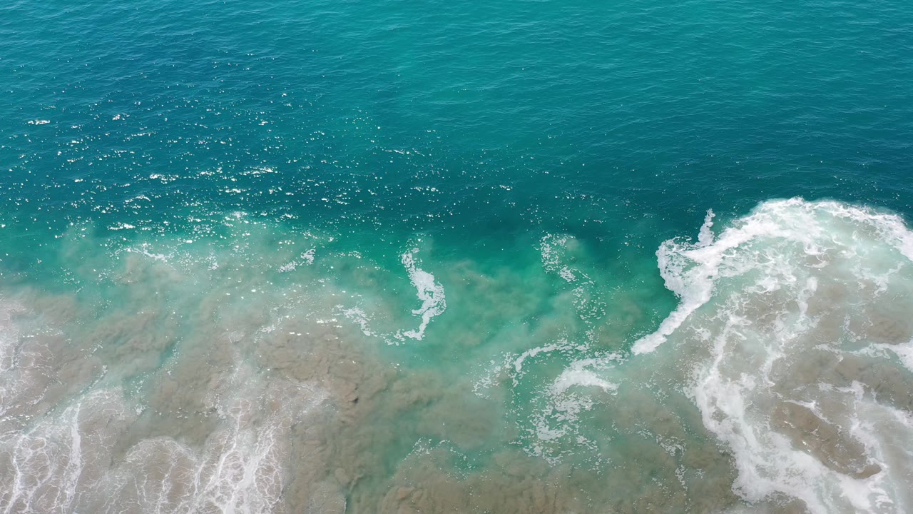Aerial surf line with bright foam and blue-green water.