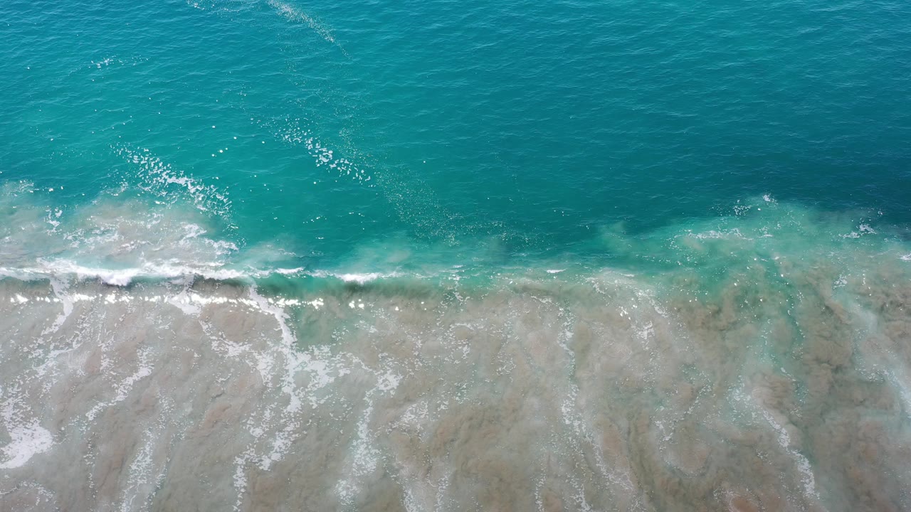 Foamy wave breaking across shallow beach water.