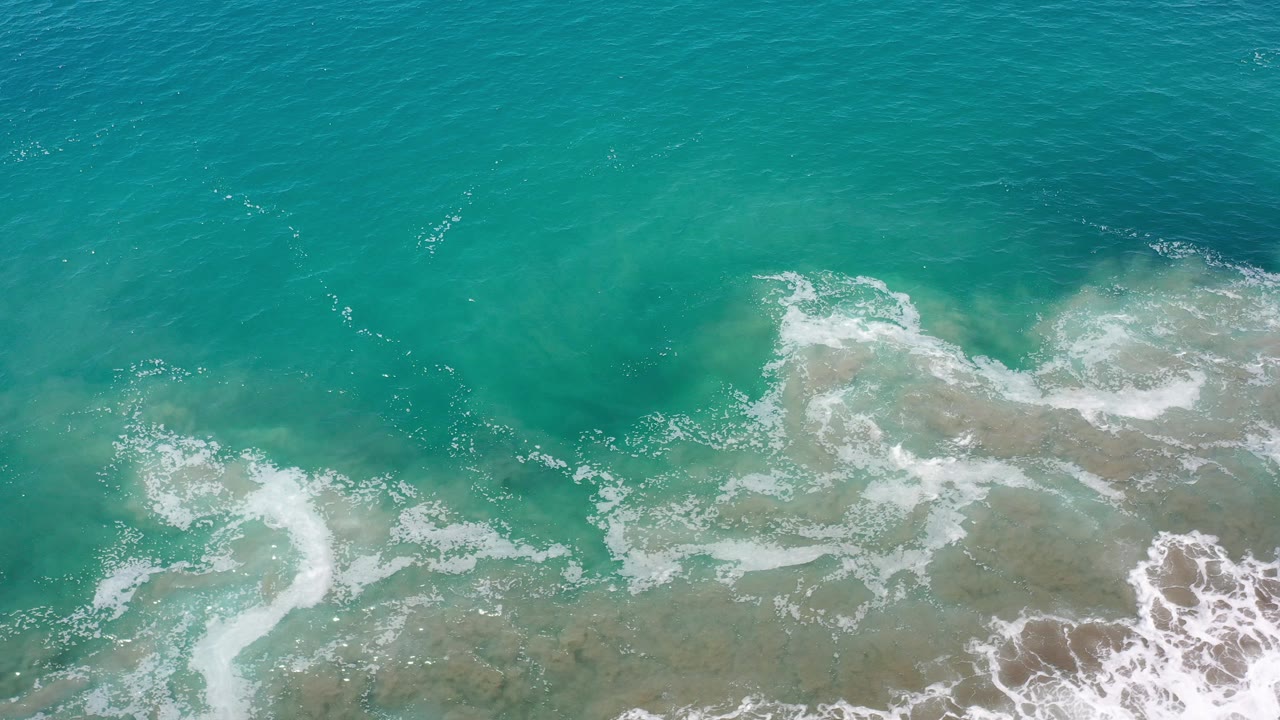 Overhead turquoise sea with white foam over shallow water.