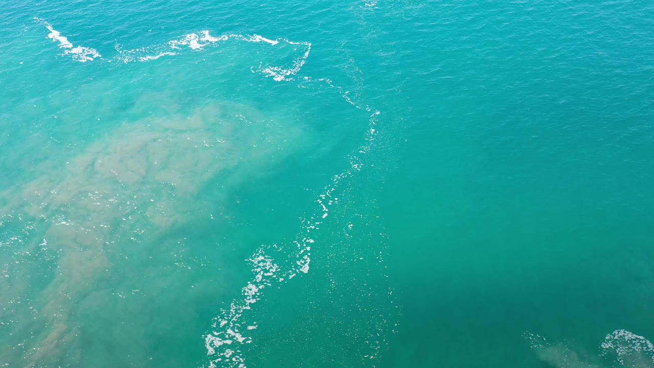 Overhead turquoise ocean with pale submerged formations and white foam.