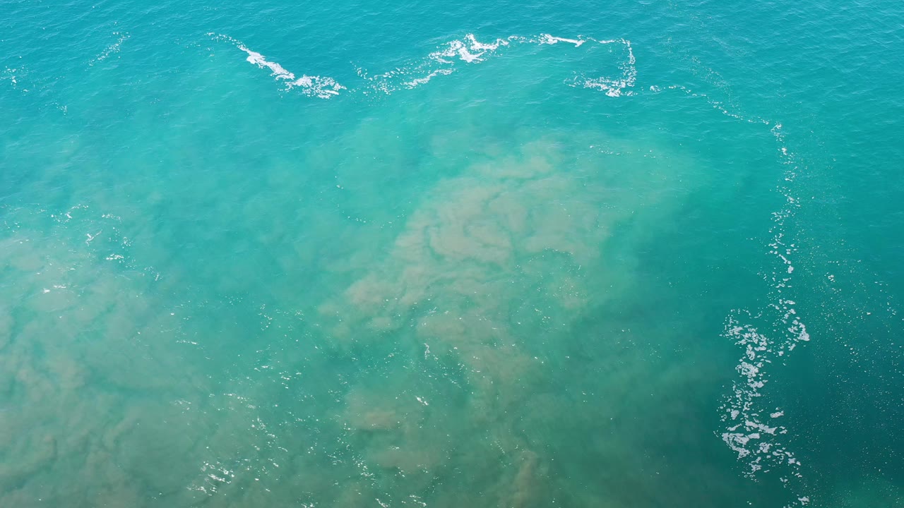 Turquoise water seen from above with a darker patch and foam at the upper edge.