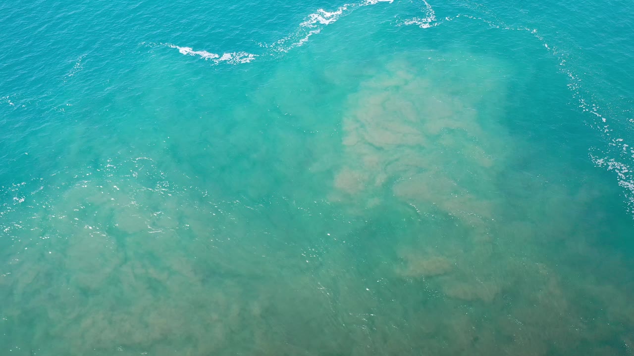 Turquoise ocean with cloudy tan sand shapes below the surface.