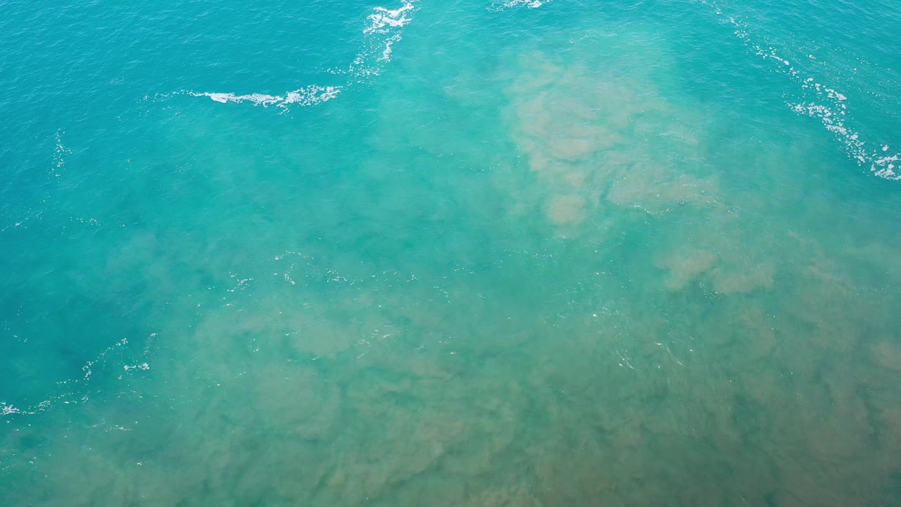 Turquoise ocean water with pale sand visible below and small white wave streaks near the top.