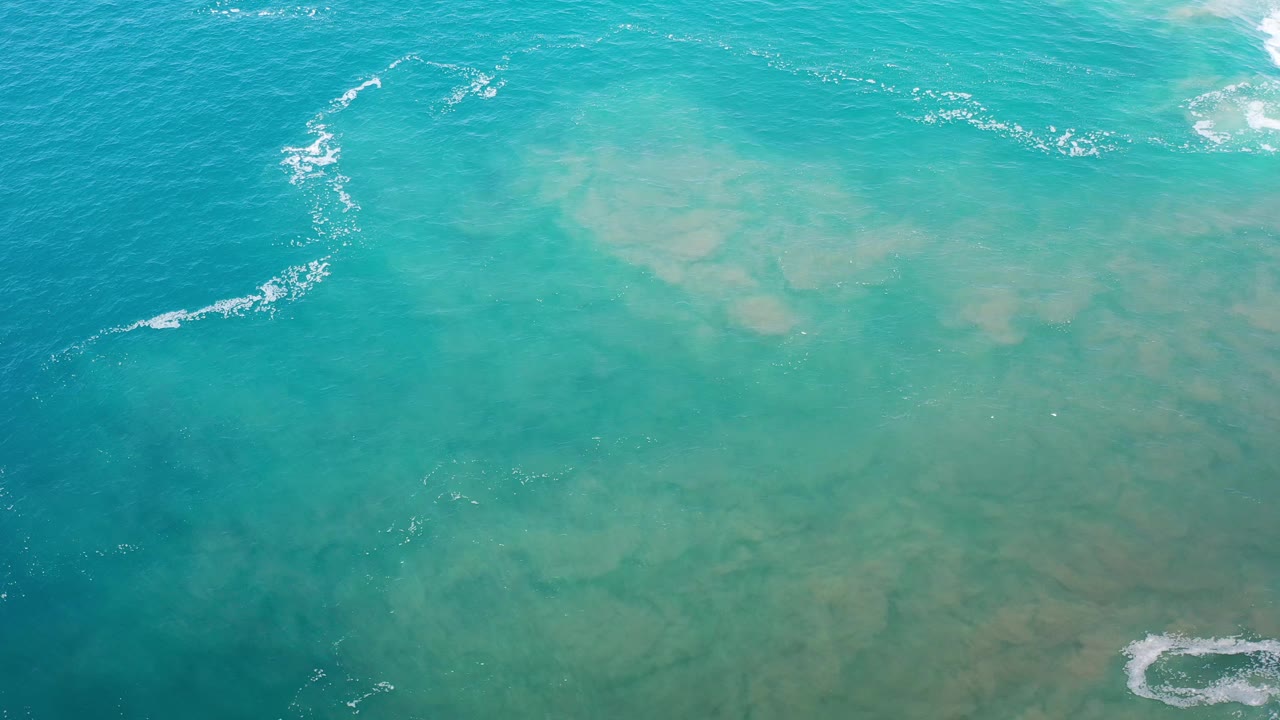 Top-down green-blue ocean with cloudy underwater color and small surf patches.