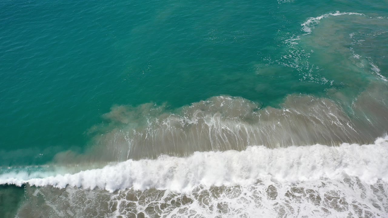 Overhead view of emerald water and white surf crossing sandy shallows in Los Cabos, Mexico, with no visible people.