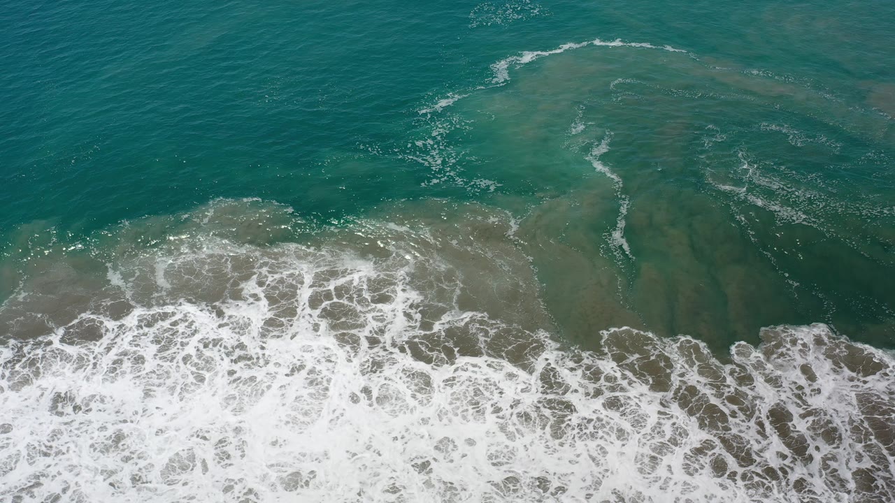 Overhead ocean surface with curved foam lines and darker green patches.