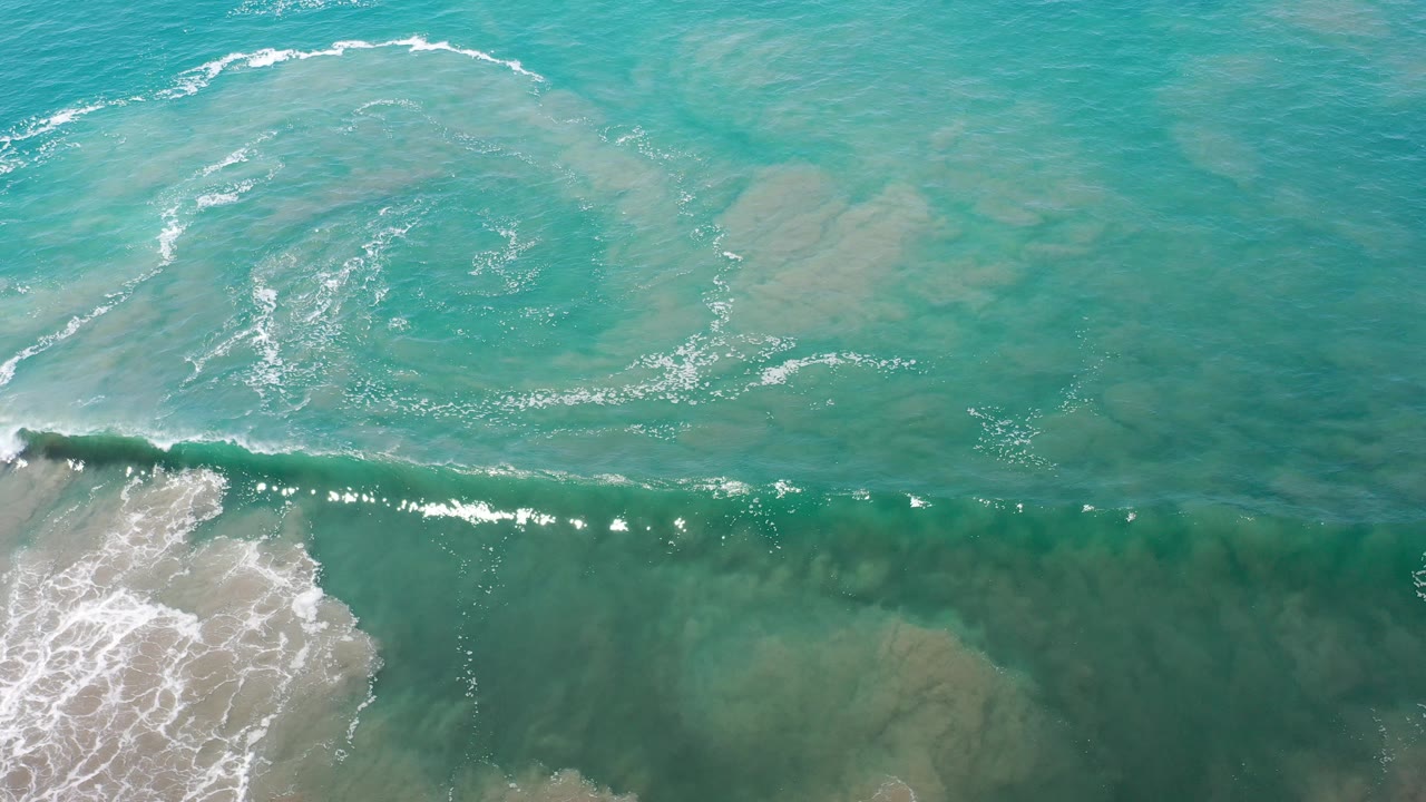 Overhead view of blue-green ocean water in Los Cabos, Mexico, with a white surf line entering along the lower edge and no visible people.