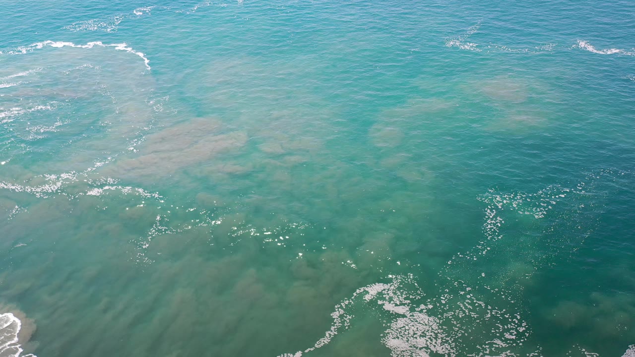 Turquoise ocean surface with foam flecks and sandy water patterns.