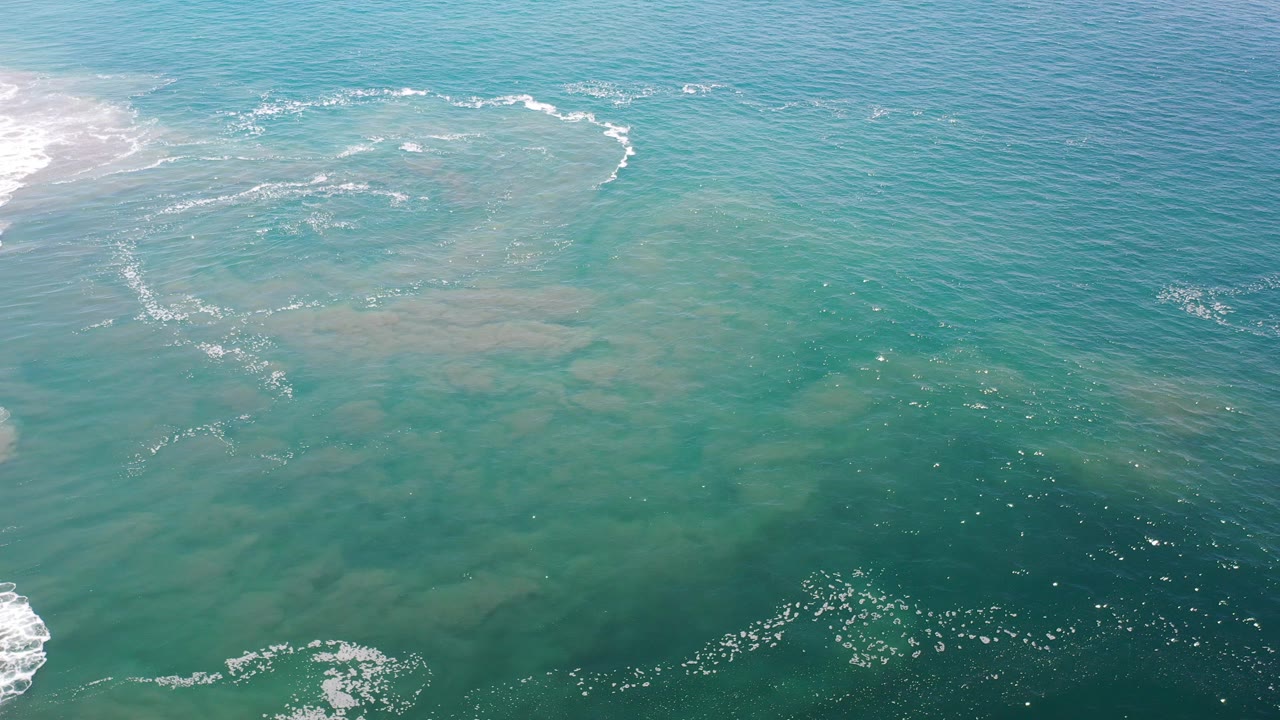 Overhead turquoise ocean with foam lines and pale underwater sand patches