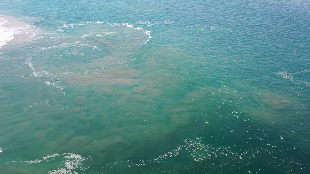 Turquoise sea surface with pale shallows and small foam clusters