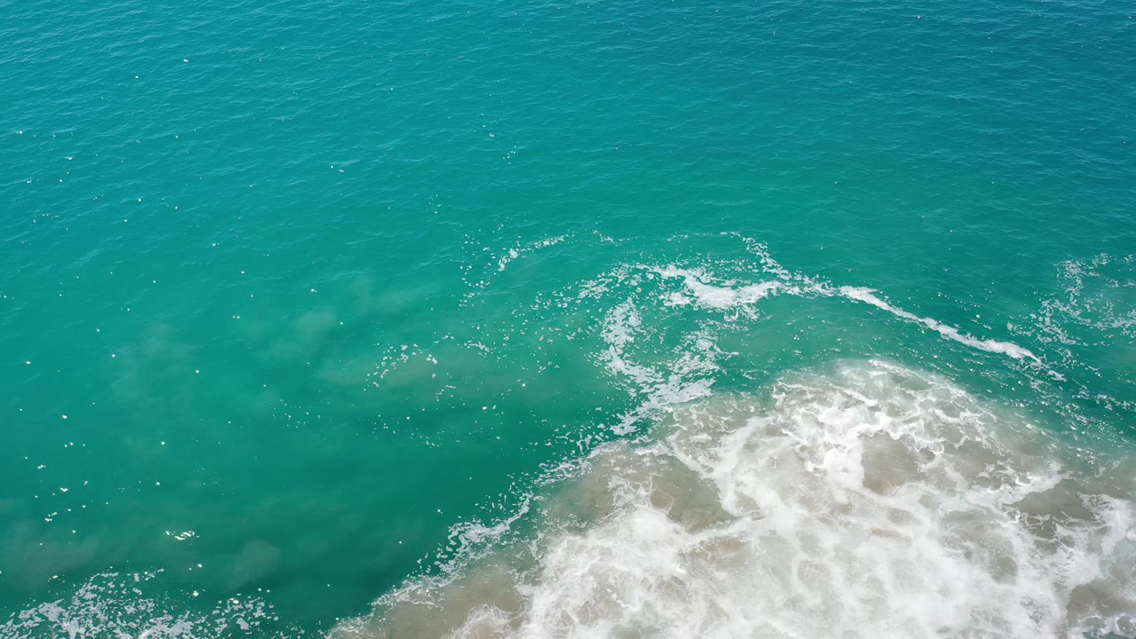 Breaking white water curls through shallow turquoise sea.
