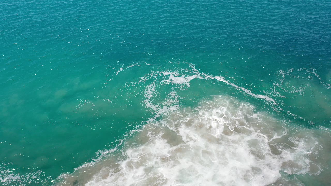 Opening overhead view of turquoise water and white surf over shallow brown-green patches in Los Cabos, Mexico, with no visible people.