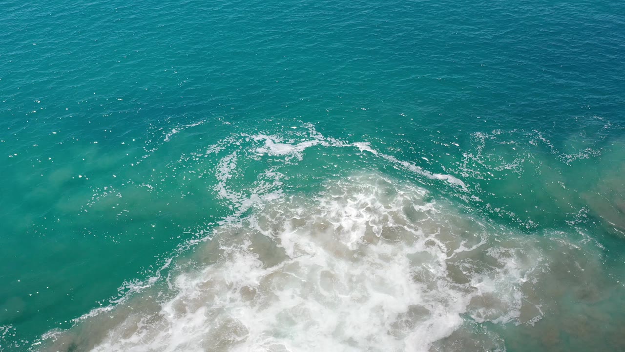 Aerial view of surf foam moving over shallow coastal water.