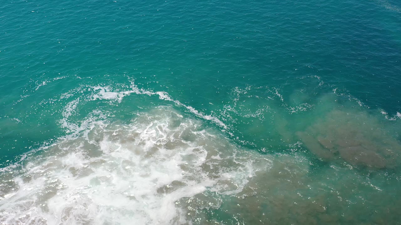 Aerial frame from Los Cabos, Mexico showing a broad patch of white foam over blue-green water with darker open sea above and no visible people.