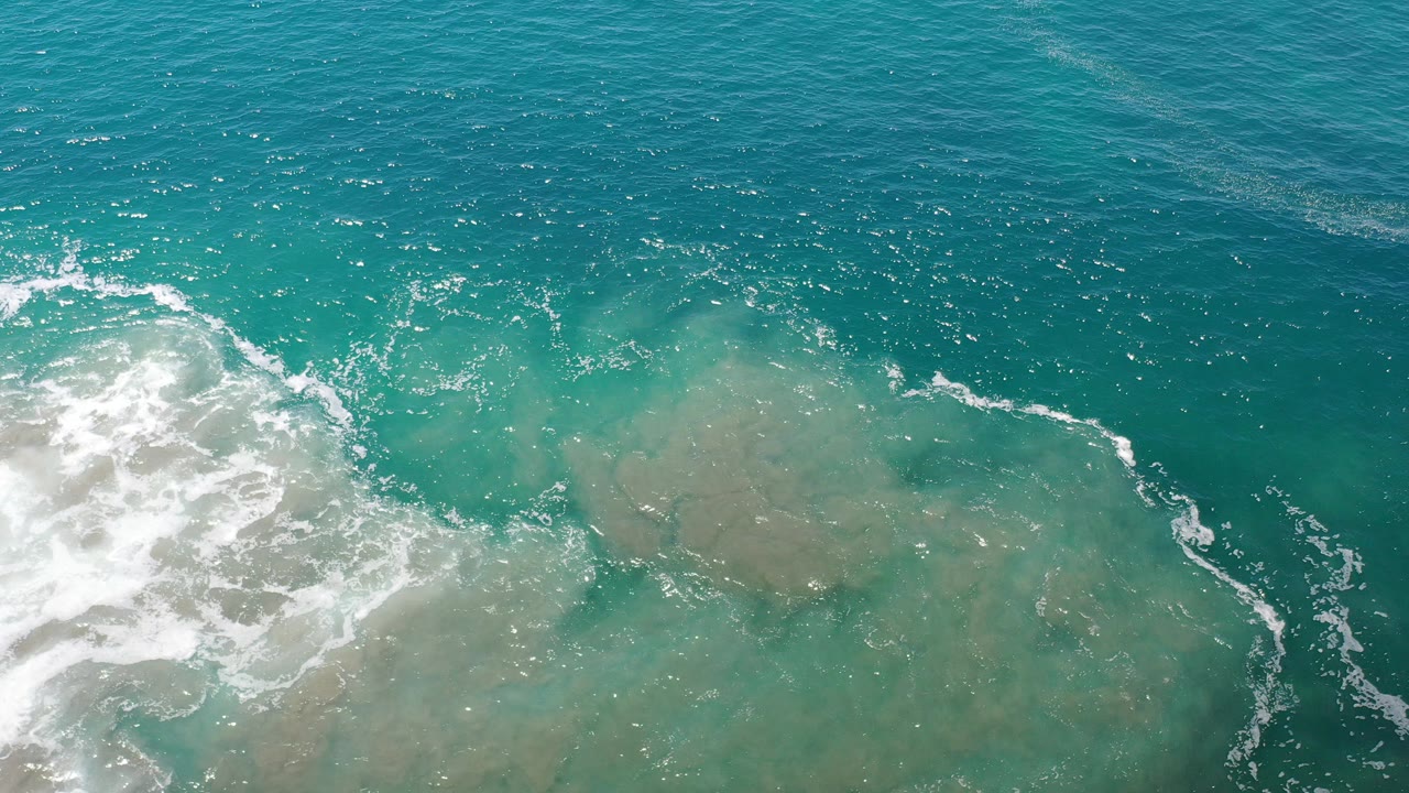 Turquoise ocean water with white surf and pale reef below.