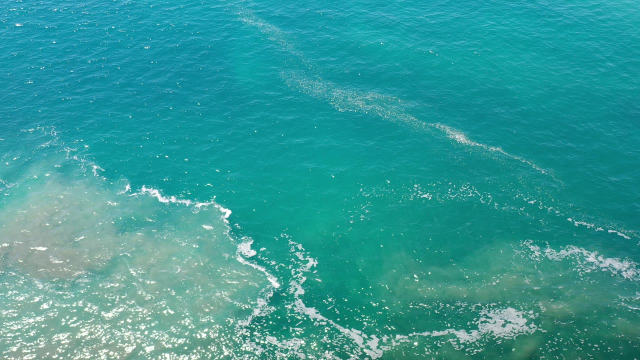 Overhead view of turquoise sea water and white foam over sandy shallows in Los Cabos, Mexico, with no visible people.