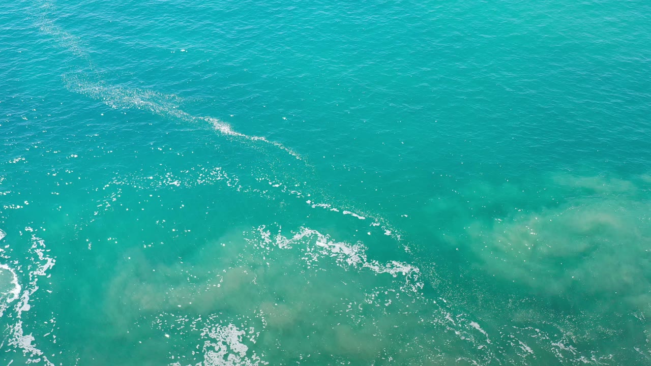 Turquoise sea surface with white foam curving over pale underwater sand.