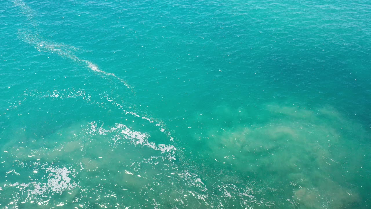 Top-down view of turquoise ocean water in Los Cabos, Mexico, with bright sun sparkle near the lower left and no visible people.