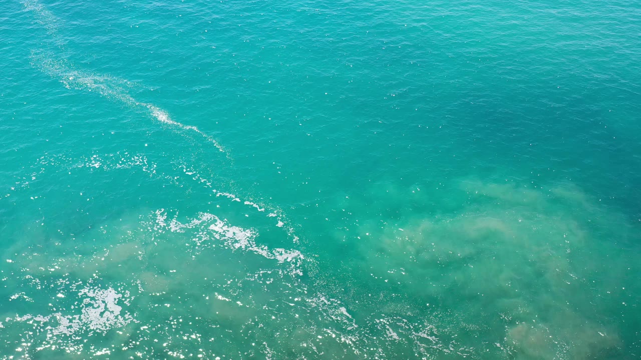 Overhead Los Cabos ocean surface with a pale diagonal streak across blue-green water and no visible people.