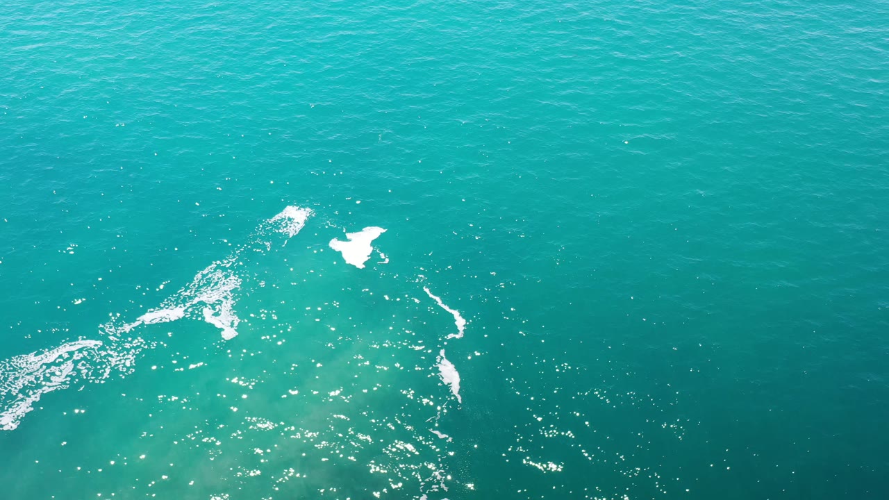 Turquoise ocean with bright foam and sun glints.