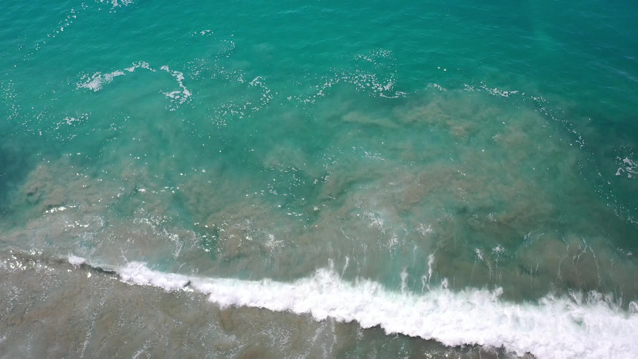 Bright turquoise sea with foam breaking along the shore.