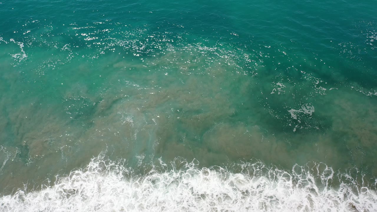 Aerial view of turquoise water and white wave wash near the bottom.