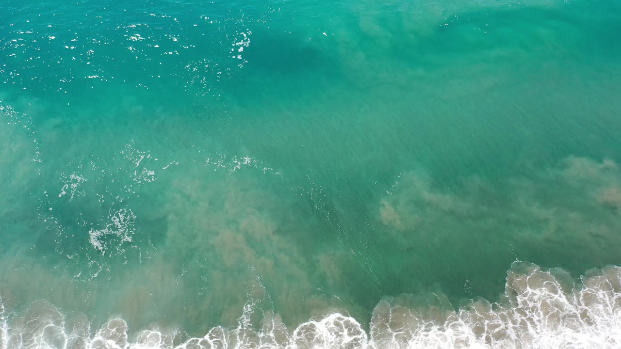 Top-down clear ocean with breaking foam and bright water reflections