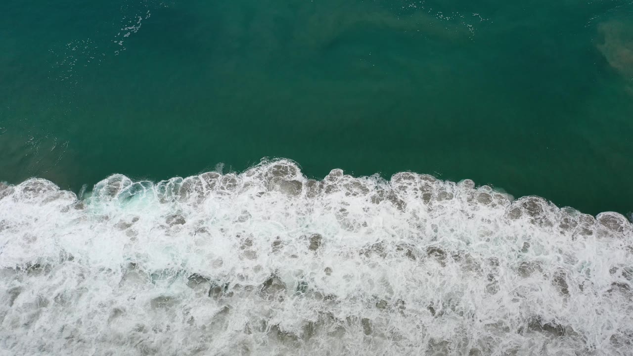 Dense white surf divides clear green water in an overhead view.