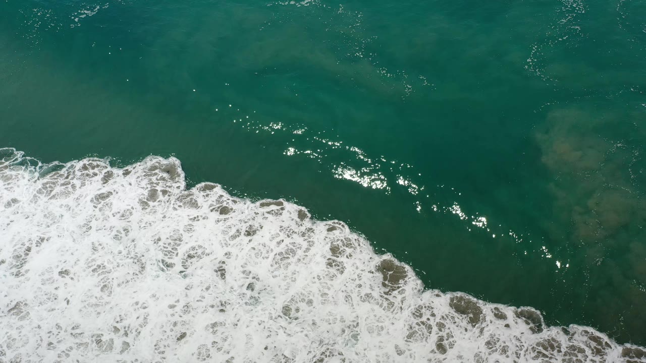 Aerial-looking frame of Los Cabos green ocean water where white surf pushes farther into the lower center, with no visible people.