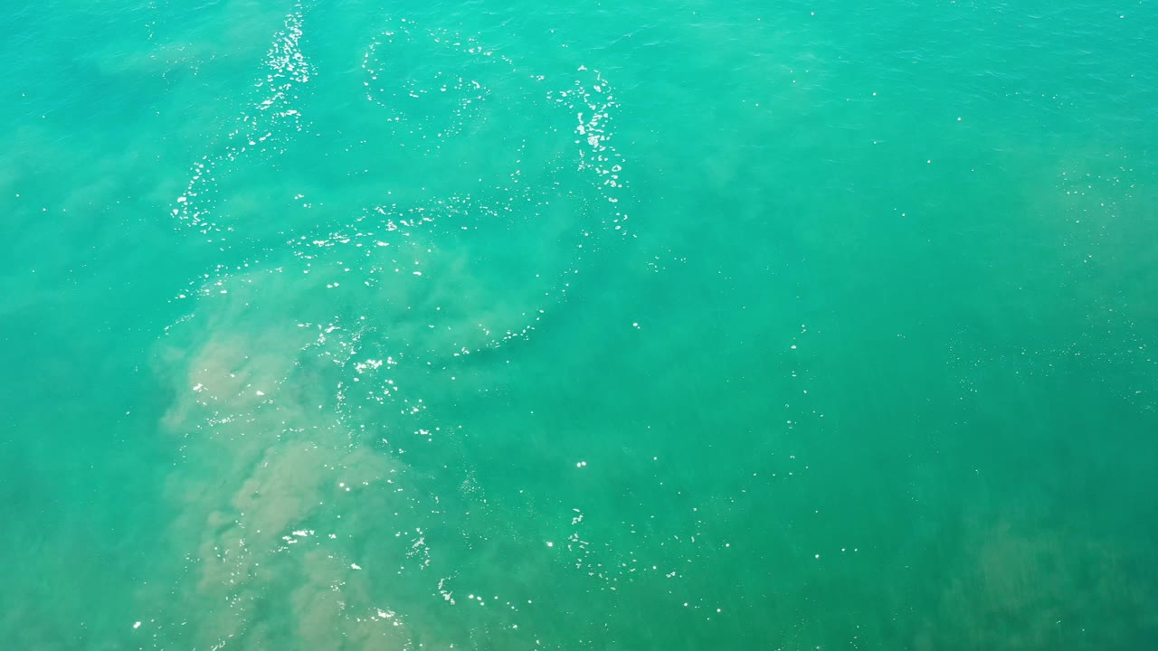 Blue ocean water from above with a pale submerged area and small white ripples.