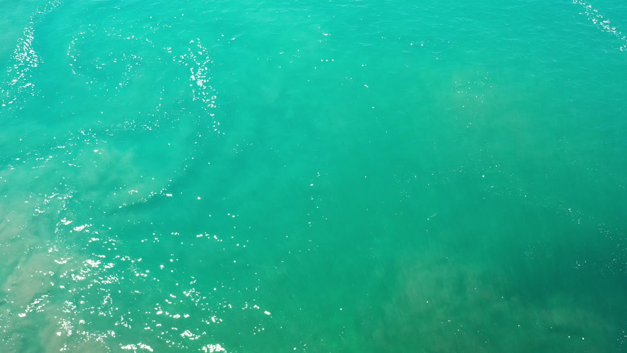 Direct overhead view of turquoise water in Los Cabos, Mexico, with bright reflections near the left edge and no visible people.